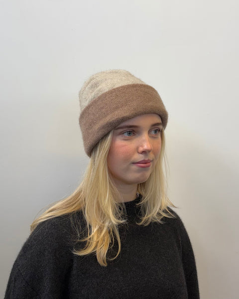 Person wearing a two-tone beige beanie with a plain background