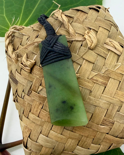 Greenstone pendant with black bound cord on a woven flax bag