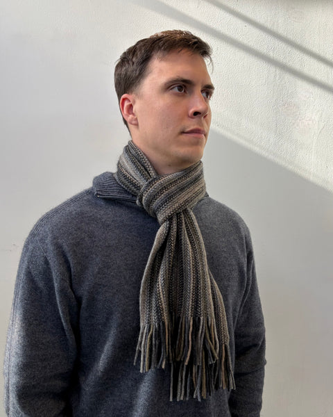 Man wearing a grey sweater and beige knitted scarf against a white wall