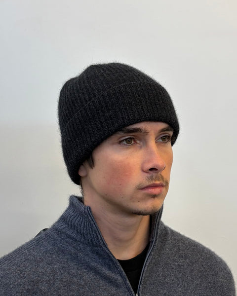 Man wearing a dark grey knit beanie against a plain background