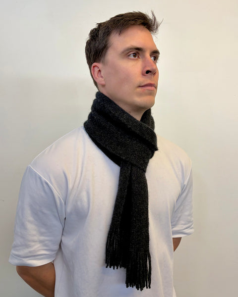 Man wearing a dark grey scarf around his neck against a plain background
