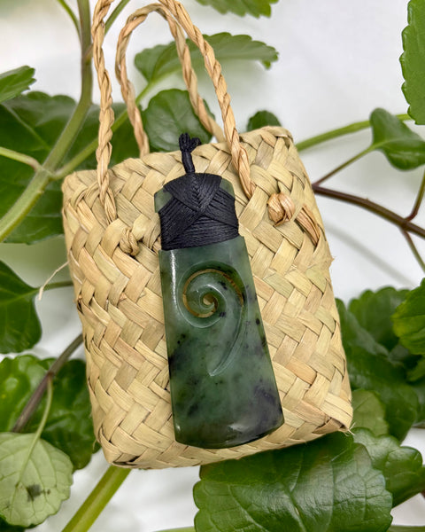 Greenstone pendant with a spiral design on a woven flax bag