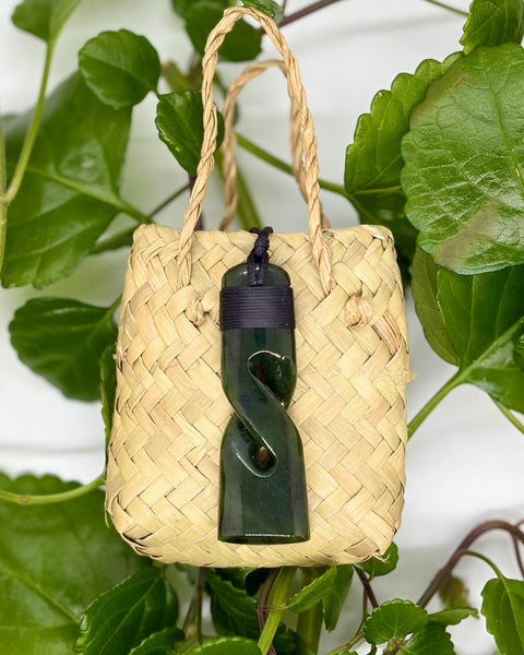 Greenstone pendant on a woven flax bag with green leaves in the background