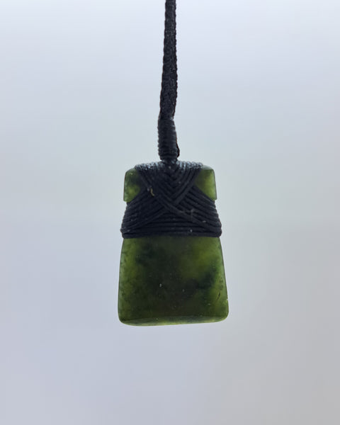 A greenstone pendant with a black braided cord wrap at the top.