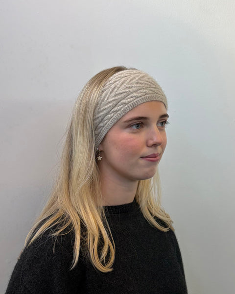 Woman wearing a beige knitted headband against a plain background