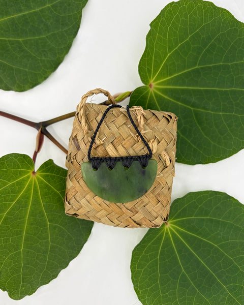 Woven basket with a greenstone pendant on a white background with green leaves