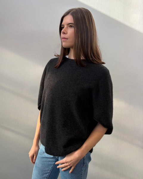 Person wearing a dark grey poncho and blue jeans against a plain background