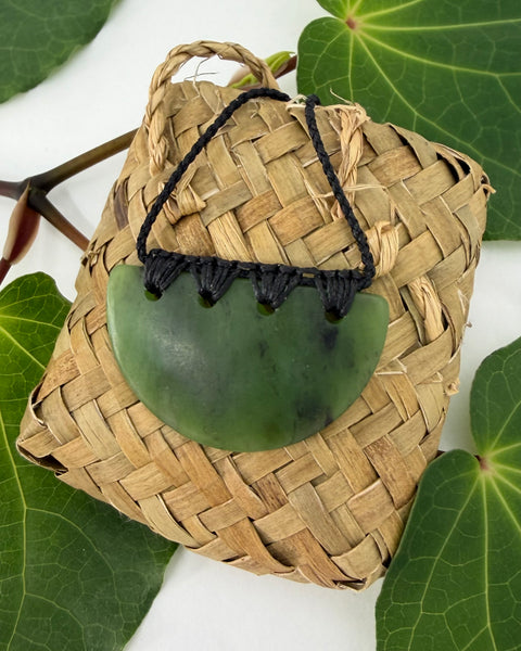 Greenstone pendant with a black cord on a woven flax bag and leafy background