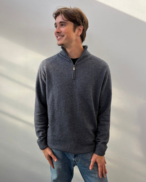 Man wearing a blue sweater and blue jeans against a plain background