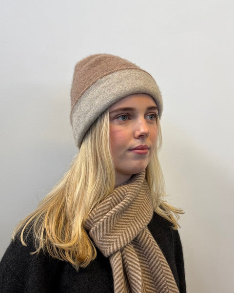 Woman wearing a two-tone beanie and scarf against a plain background