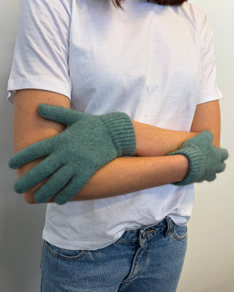 Person wearing teal gloves with a plain background