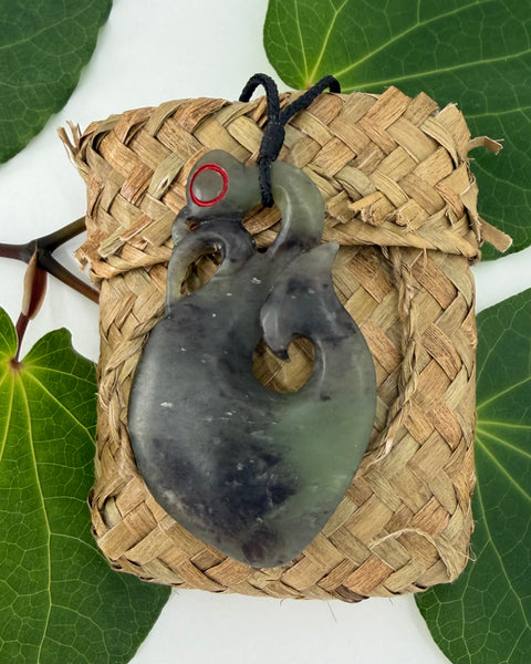 Greenstone pendant on a woven flax bag on a white background with green leaves
