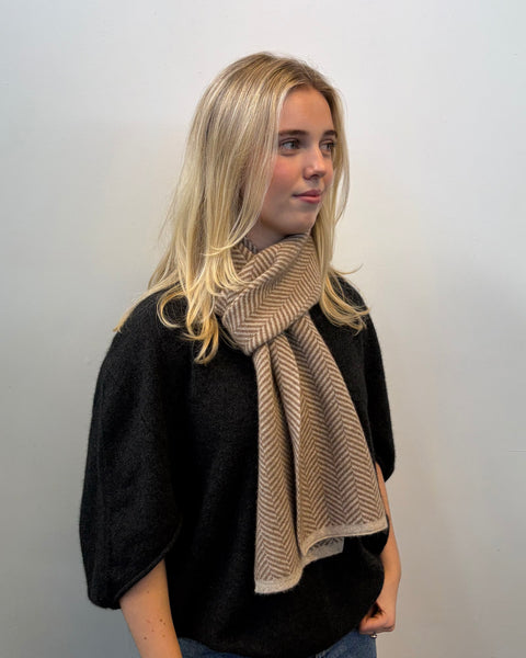 Woman wearing a beige scarf against a plain background