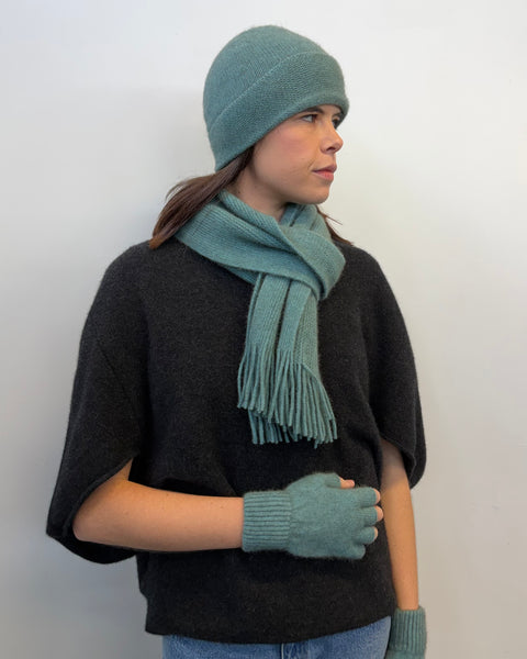 Person wearing a matching teal knit set including hat, scarf, and fingerless gloves against a white background