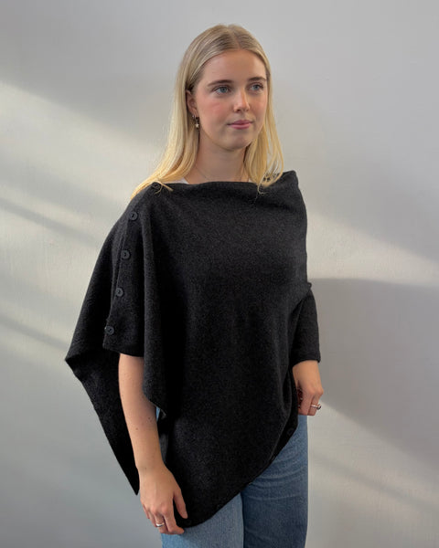 Woman wearing a dark grey poncho against a plain background