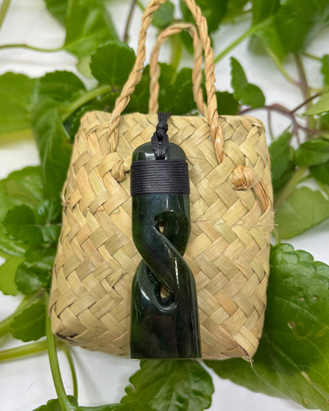 Greenstone pendant on a woven flax with green leaves in the background