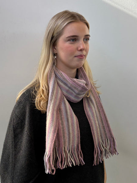 Woman wearing a pink striped knitted scarf against a plain background