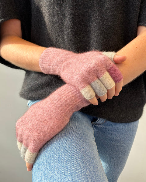 Person wearing pink knitted gloves with multi coloured tips against a white background.
