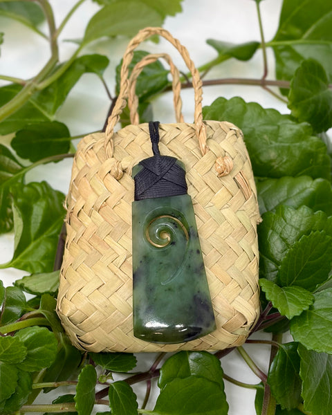 Greenstone pounamu pendant with a black cord on a woven flax bag
