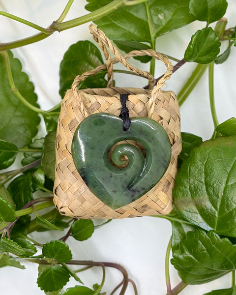 Greenstone heart pendant with spiral centre on a woven flax bag