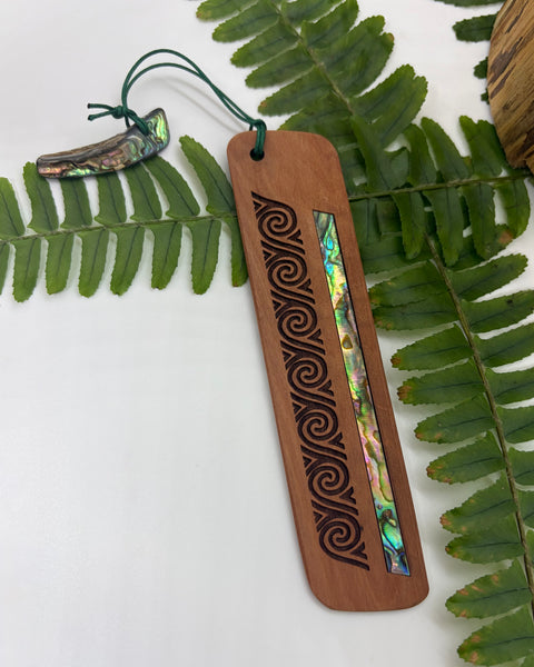 Wooden bookmark with paua shell inlay on a white background with green leaves.