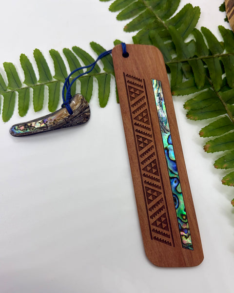 Wooden bookmark with paua shell inlay on a white background with green leaves.