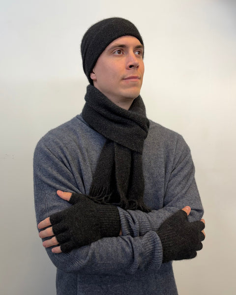 Man wearing a matching set of dark grey beanie, scarf, and fingerless gloves against a white background