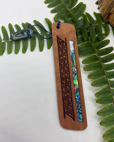 Wooden bookmark with paua shell inlay on a white background with green leaves