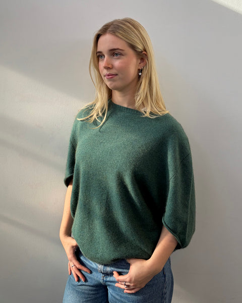 Woman wearing a teal poncho and blue jeans against a plain background