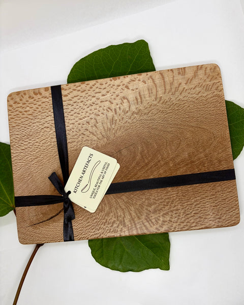 Wooden cutting board with a black ribbon and tag on green leaves