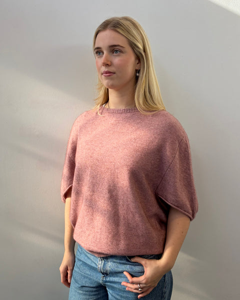 Woman wearing a pink poncho and blue jeans against a plain background