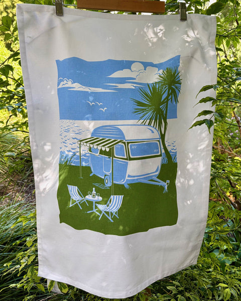 Tea Towel with a graphic of a caravan parked by the beach and an outdoor furniture setup.