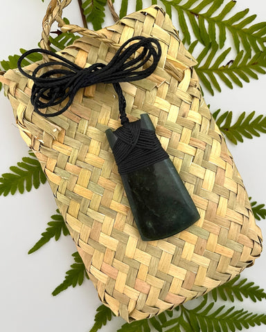 New Zealand Greenstone Toki pendant with a black handwoven cord, presented with a flax kete bag. Pounamu sourced from South Island Aotearoa and hand carved by a Master Carver in Greymouth.