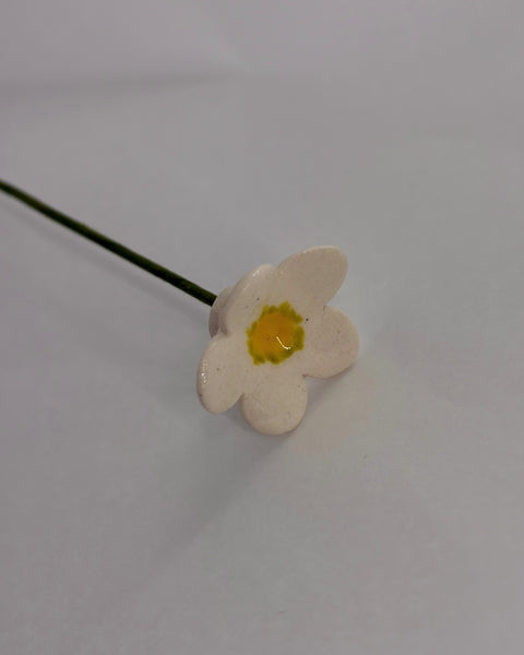 Small, white ceramic flower with a yellow centre and a green stem.