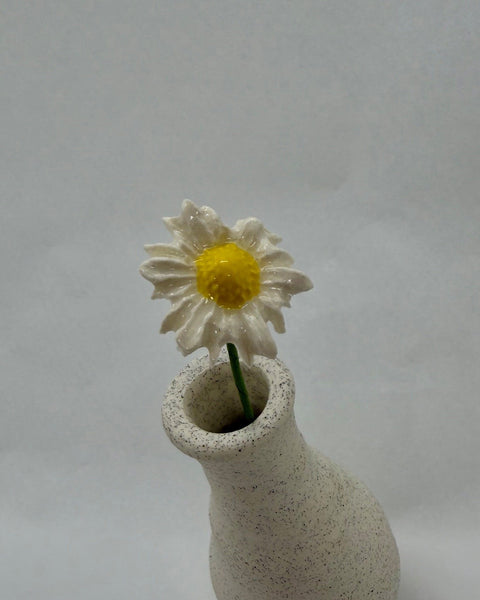 White ceramic flower with a yellow center in a white speckled vase.