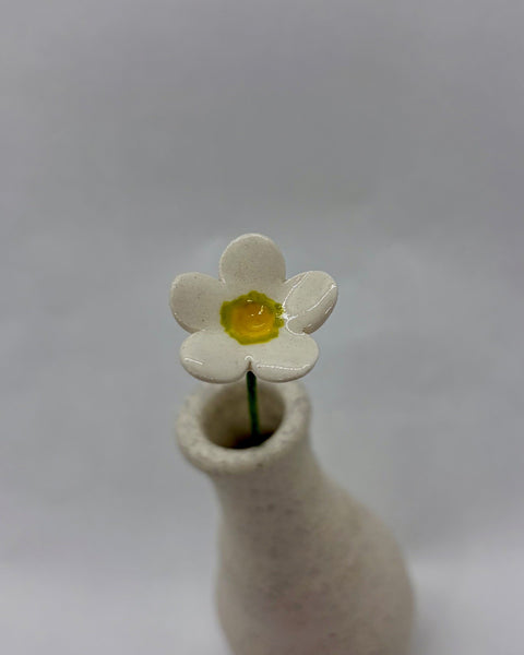 White ceramic flower with a yellow and green centre displayed in a white speckled vase.