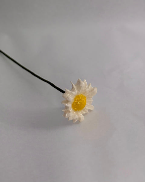 White ceramic daisy with a yellow centre and green stem.