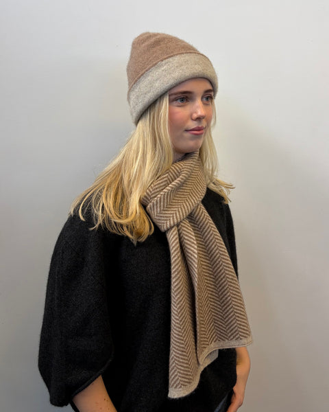 Woman wearing a beige and brown beanie and scarf against a plain background