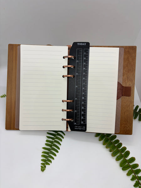 Open notebook with wooden cover on a white background with green leaves