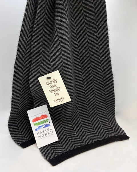 Black and grey herringbone patterned knitted scarf with two tags on a white background