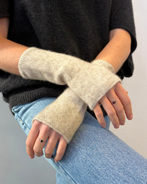 Person wearing beige wrist warmers with a dark sweater and light blue jeans