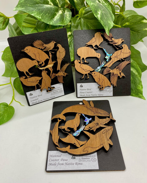 Three wooden coasters with animal designs on black packaging.