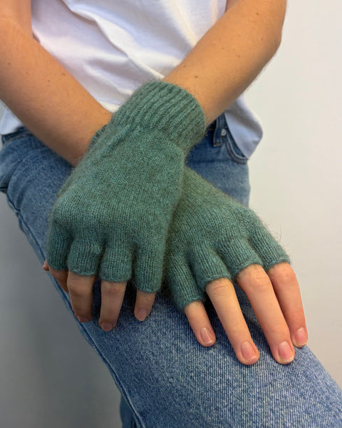 Teal fingerless gloves worn by a person sitting on a white surface