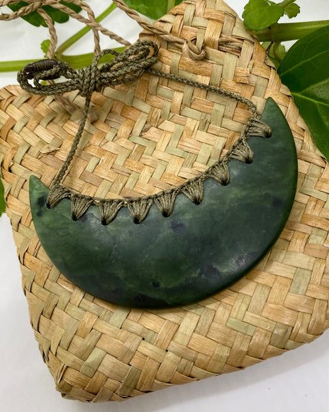 Greenstone breastplate necklace with a green woven cord on a flax woven bag