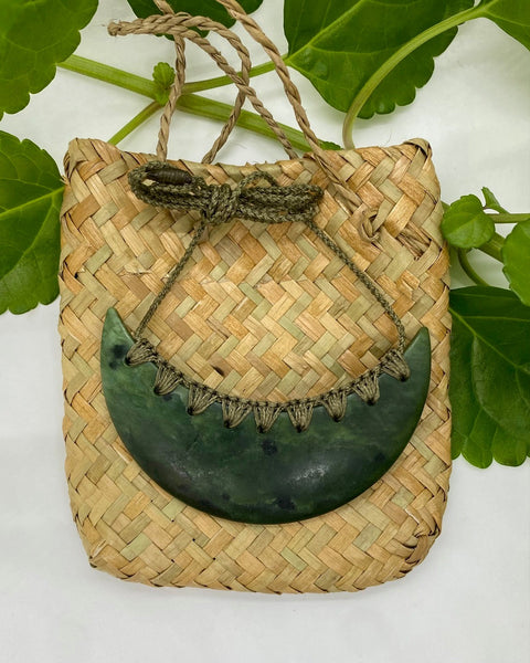 Greenstone breastplate necklace with a green woven neck cord on a flax woven bag