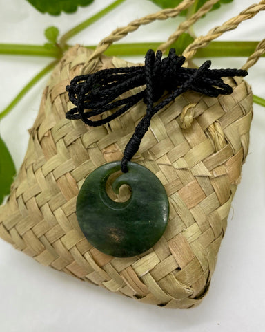 Greenstone circular pendant with spiral koru shape and black woven cord