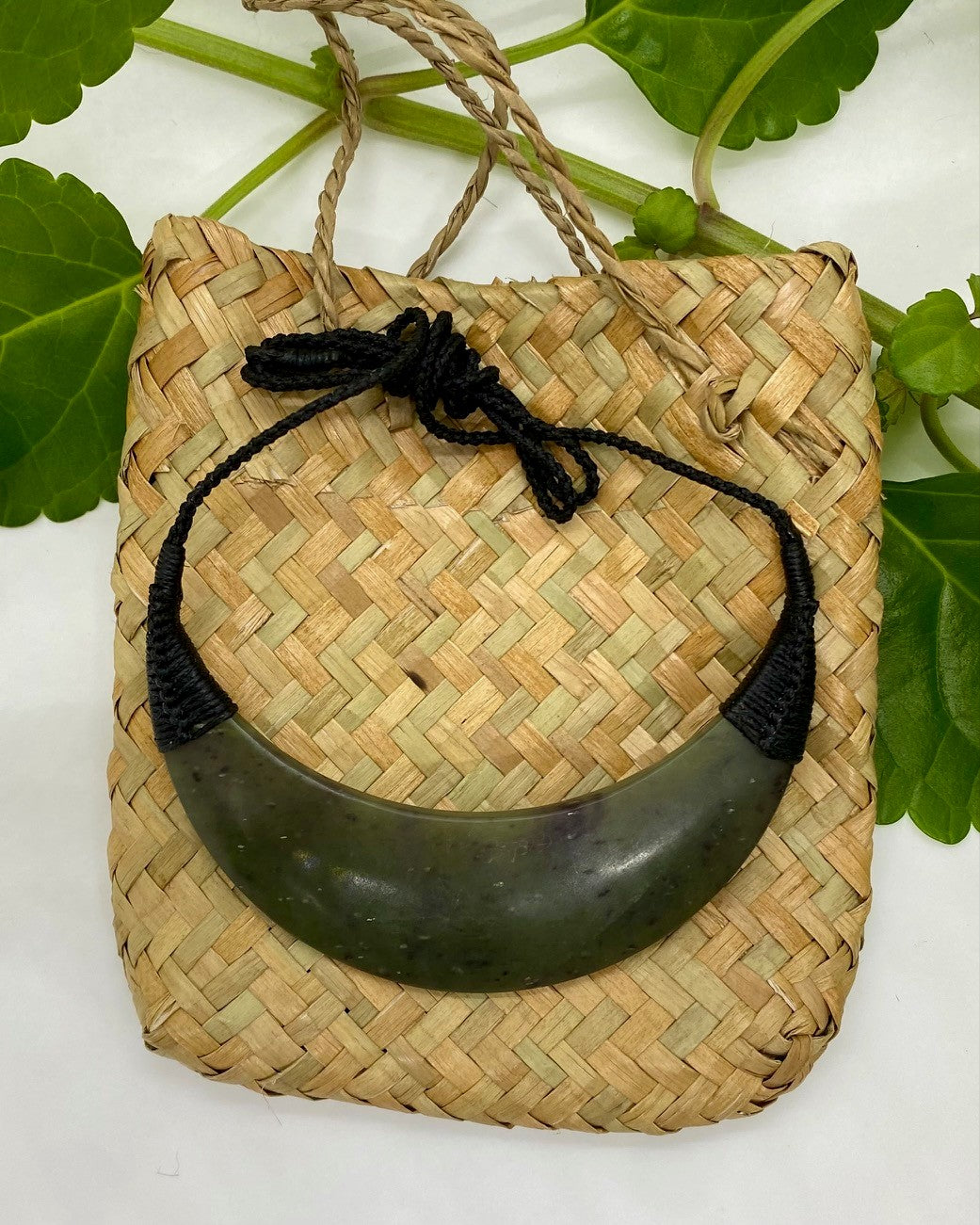 Greenstone Breastplate necklace with black woven cord on a flax woven bag