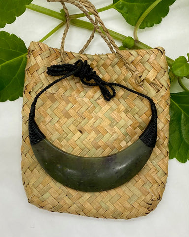 Greenstone Breastplate necklace with black woven cord on a flax woven bag