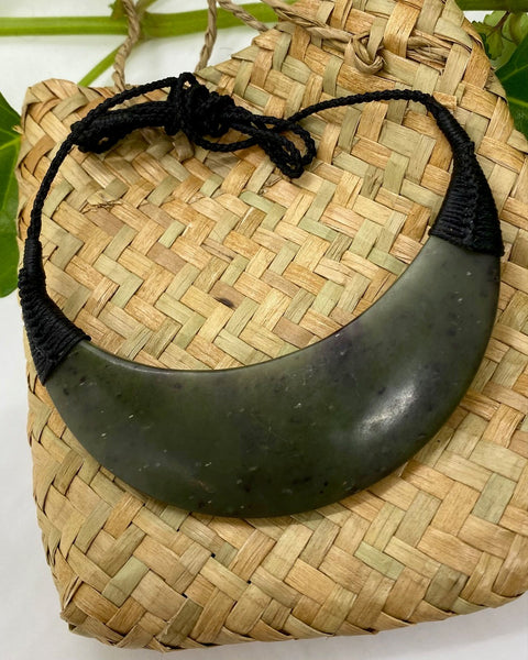 Greenstone breastplate with black woven cord on a woven flax bag