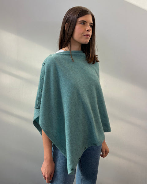Woman wearing a teal poncho against a plain background